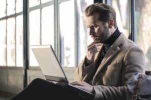 Mann, der nachdenklich auf seinen Laptop schaut und sich Gednaken über die Sinnhaftigkeit eines Hausverkaufs macht